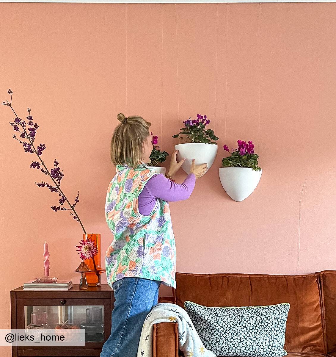 DE Blonde Frau hängt einen Botaniq-Hängeblumentopf von Artiteq an die Wand