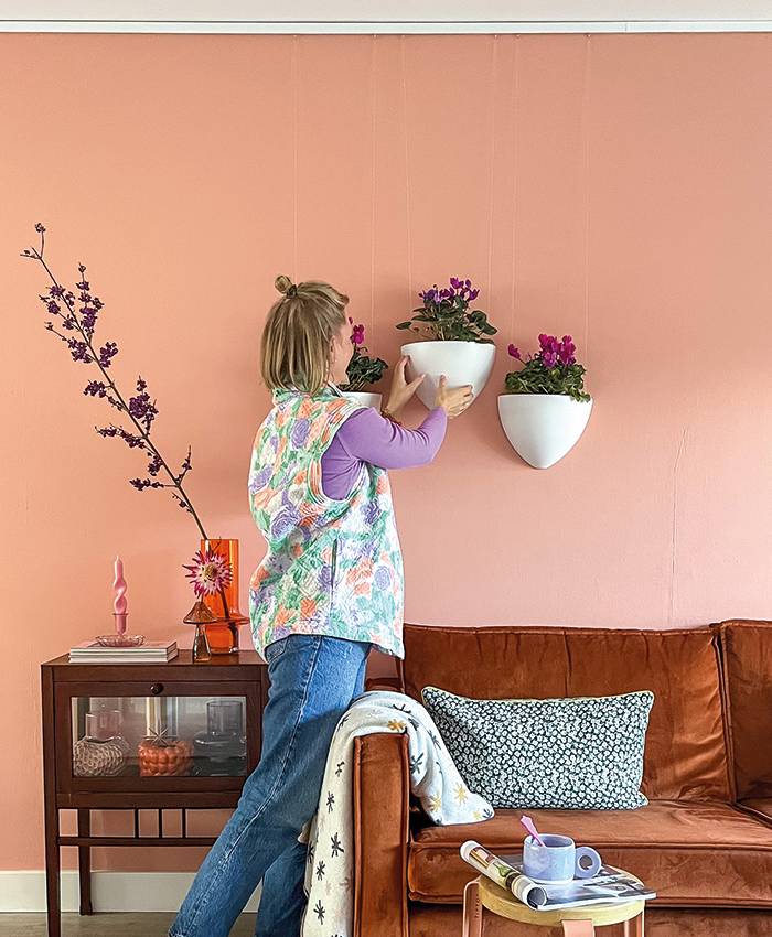 DE Blonde Frau hängt einen Botaniq-Hängeblumentopf von Artiteq an die Wand