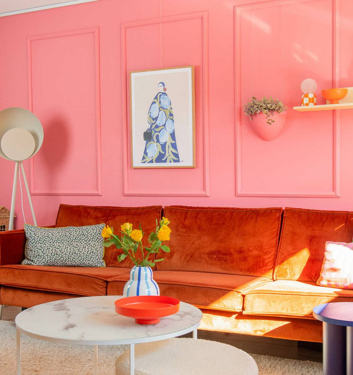 NL woonkamer met roze muur, oranje bank en kleurrijke details